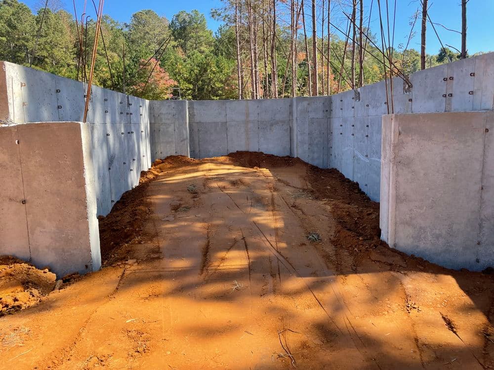 Concrete walls of a construction site with a dirt pathway, surrounded by trees.