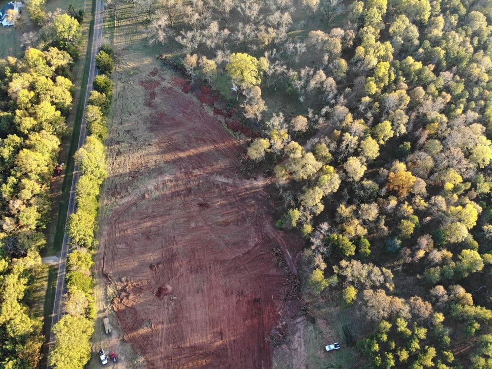 Aerial view of a cleared land area next to a dense forest with trees and a road.