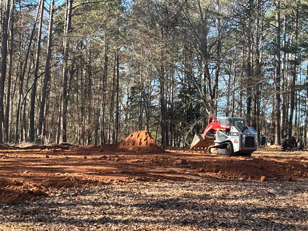 Excavator moving dirt in a wooded area, preparing land for construction or landscaping.