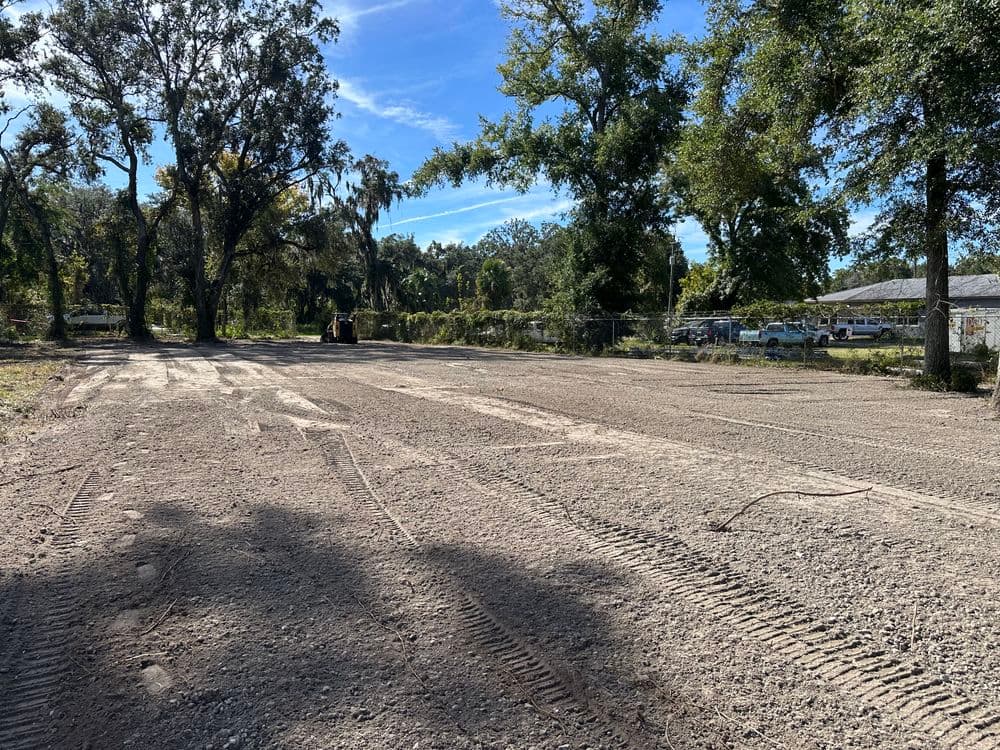 Cleared construction site with tire tracks, surrounded by trees and blue sky.