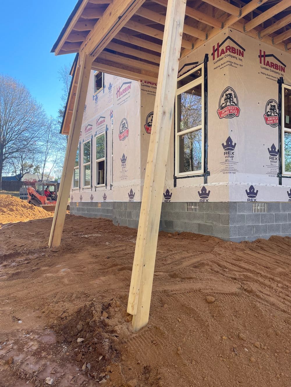 Construction site featuring a partially built house with wooden beams and sand foundation.
