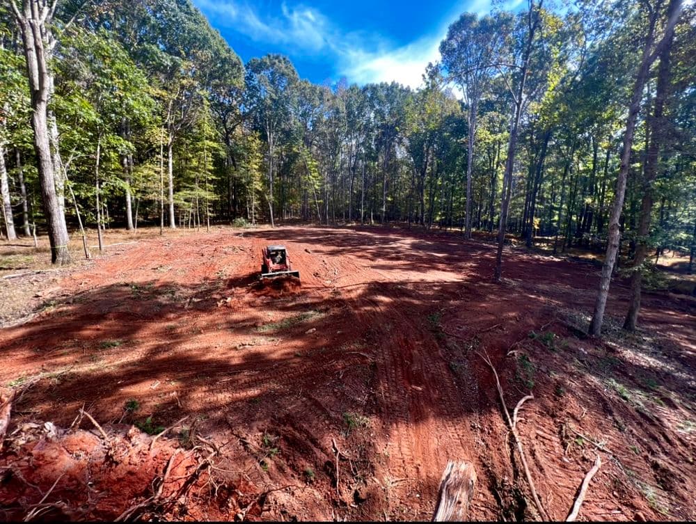 Cleared forest area with tractor, showcasing newly tilled red soil and trees in the background.