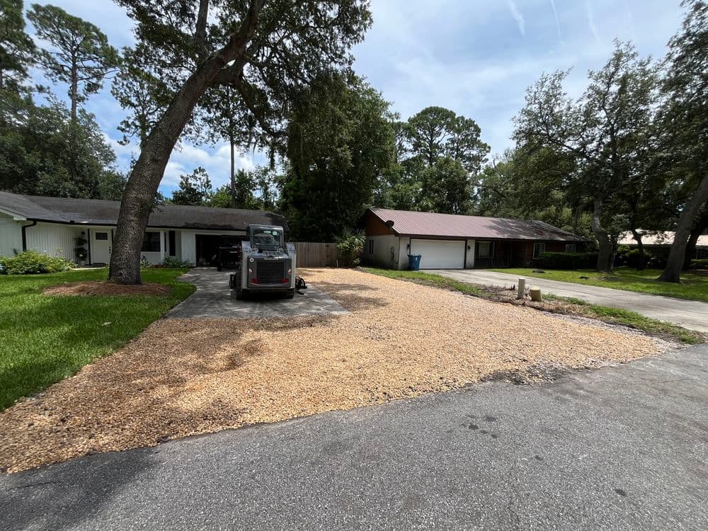 Gravel driveway and parking area in residential neighborhood with two homes.