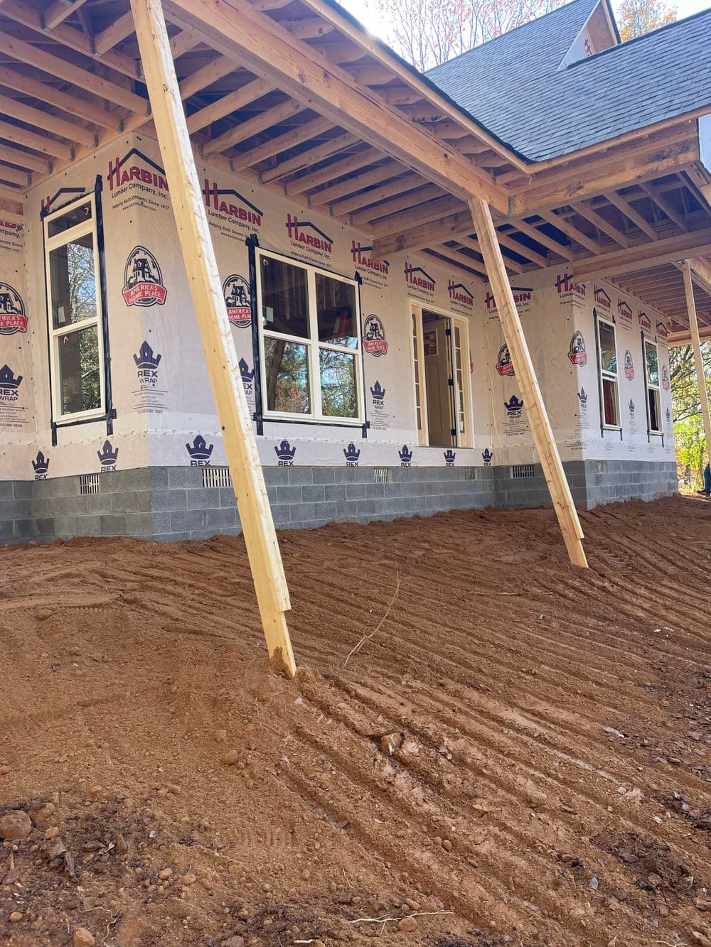 New construction home with framed walls, windows, and dirt foundation preparations.