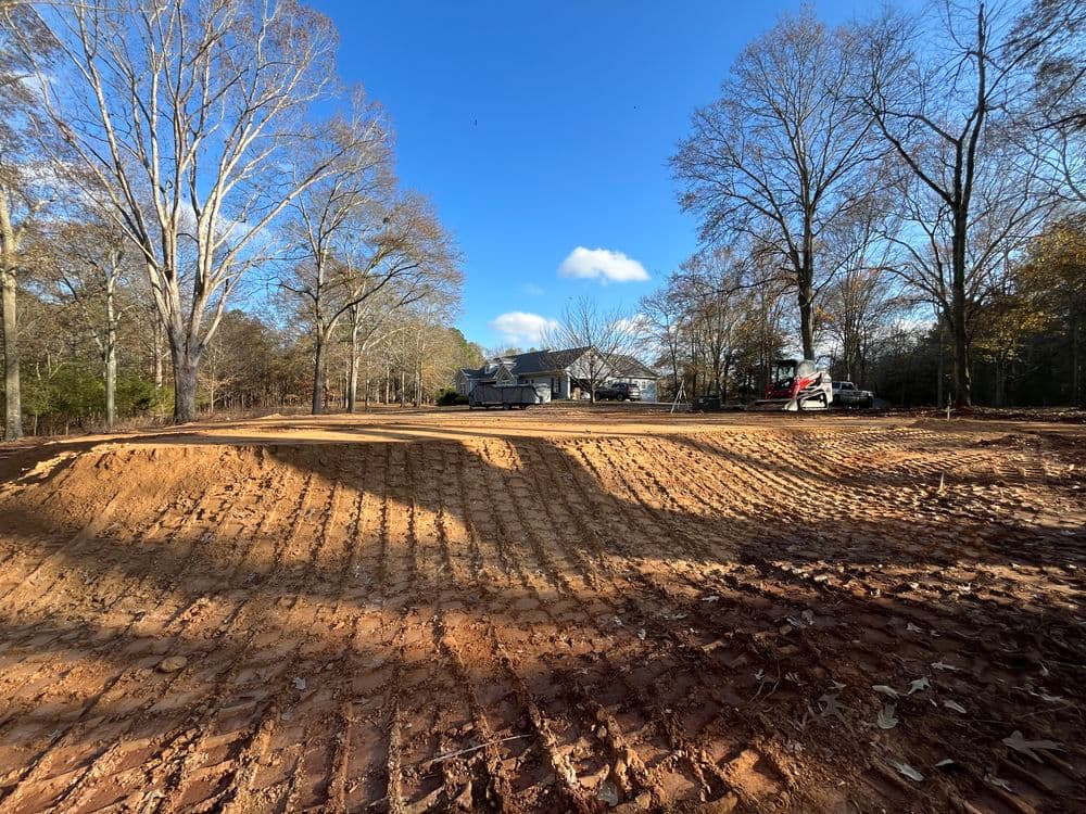 Cleared land ready for construction, with trees and machinery in the background under bright skies.