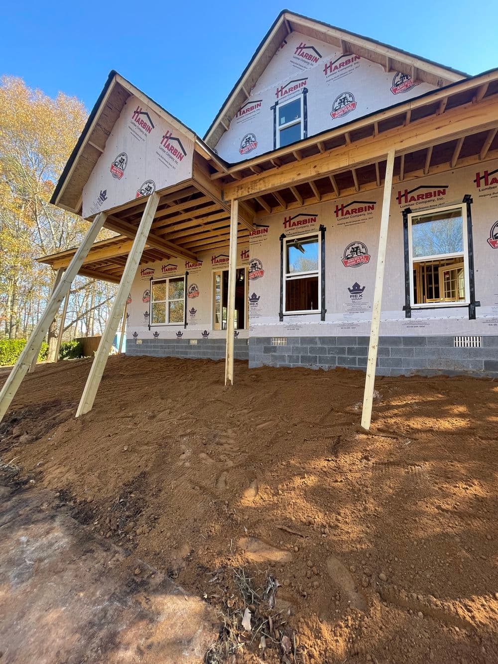 New house under construction with wooden supports and bare ground in front.