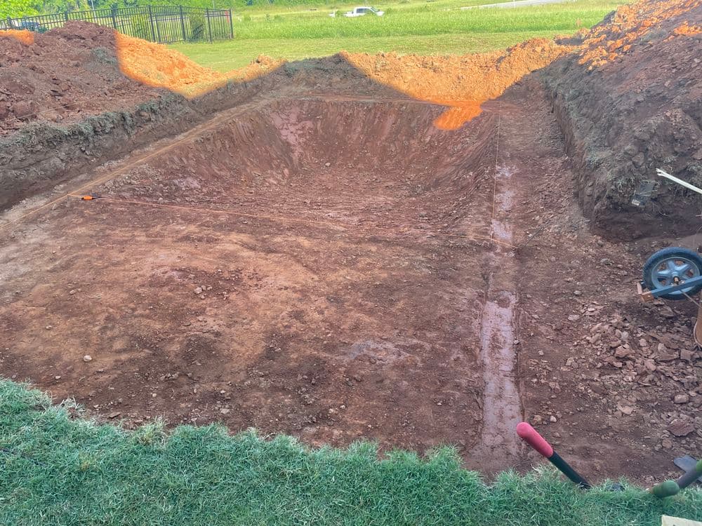Excavated dirt site for a swimming pool installation, showing shaped ground and tools.
